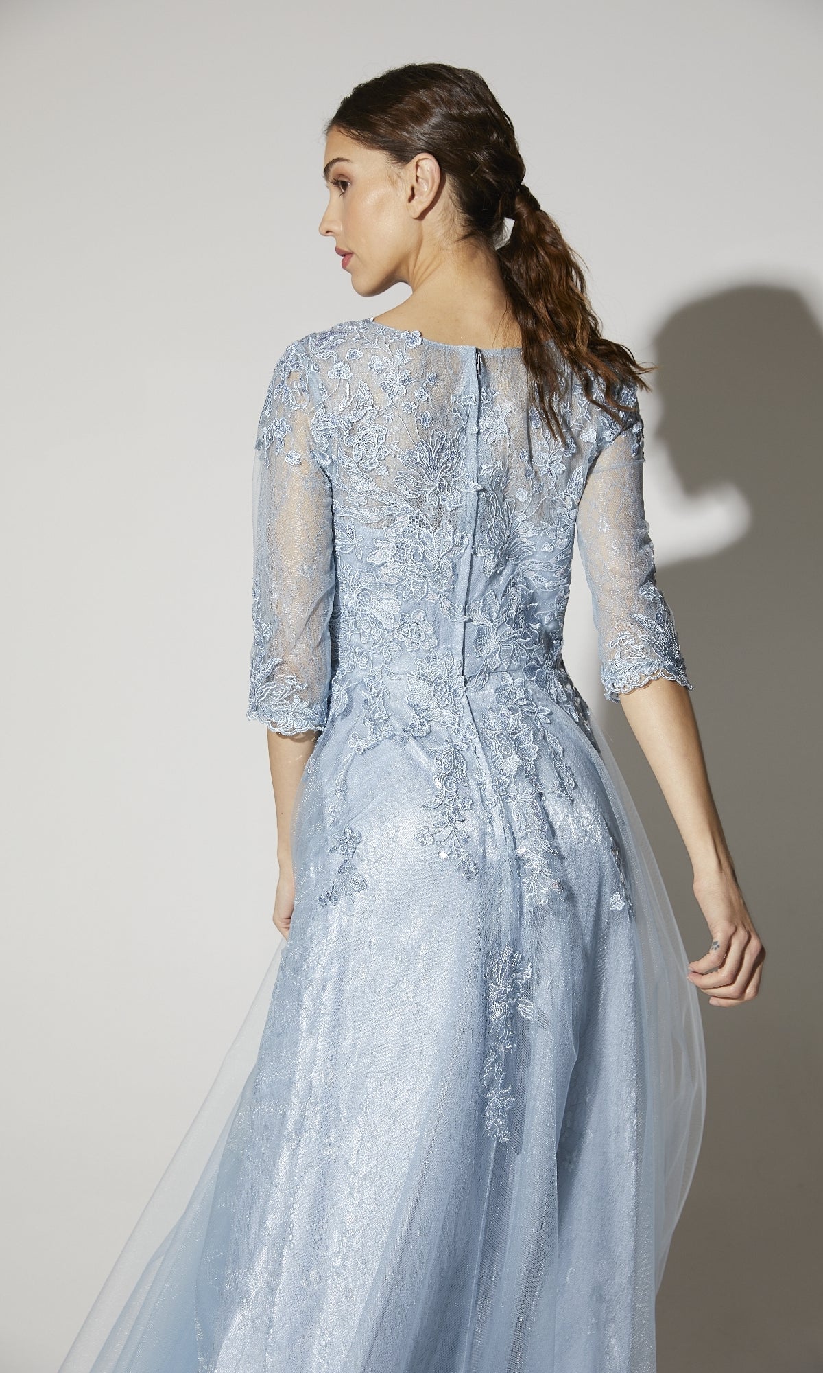 A woman, seen from the back against a plain background, wears the Eureka 9660 Flowy Long Sleeve Long Formal Dress in light blue with three-quarter sleeves and floral embroidery.
